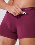 Man placing AirPods into pocket of burgundy boxer briefs with patented pocket