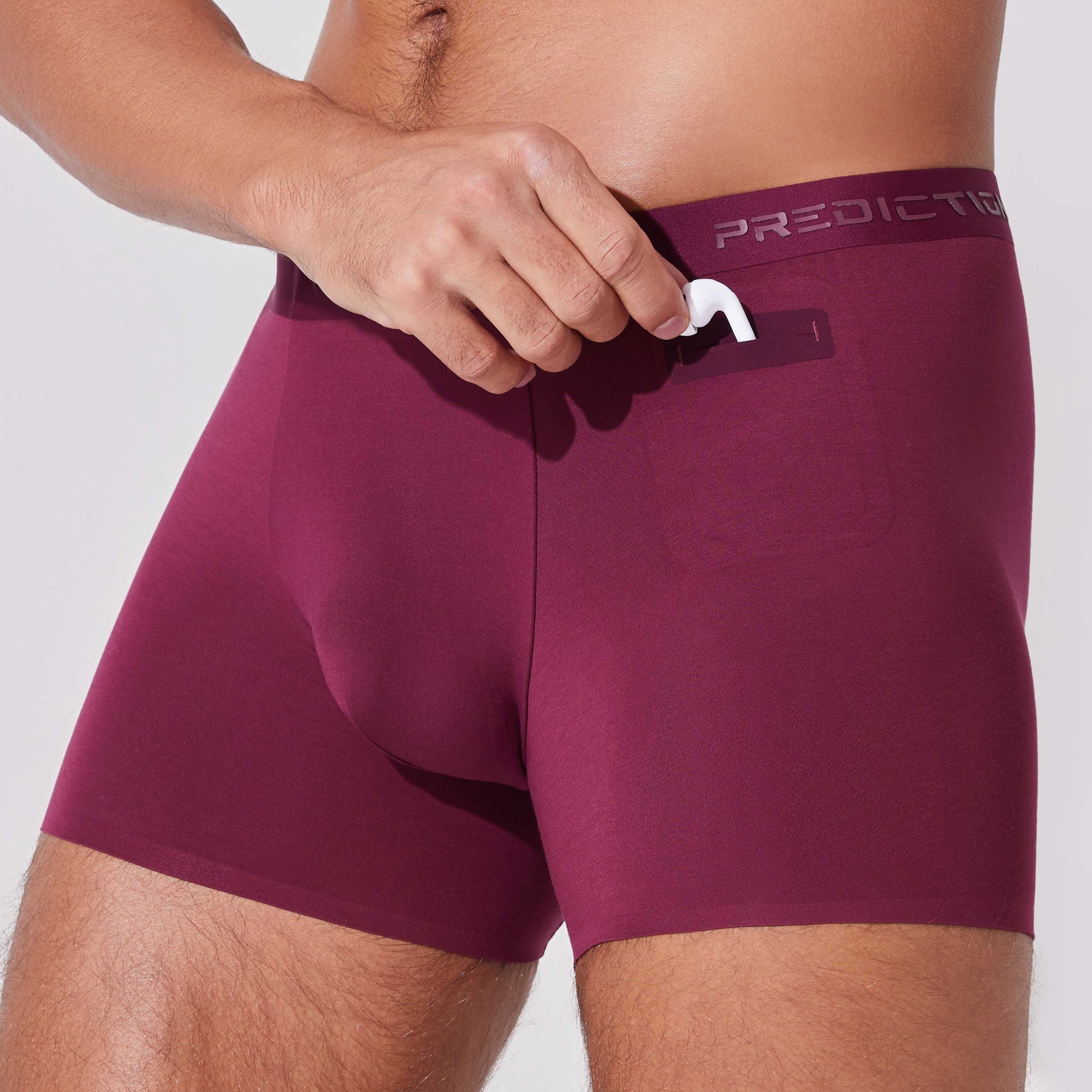 Man placing AirPods into pocket of burgundy boxer briefs with patented pocket