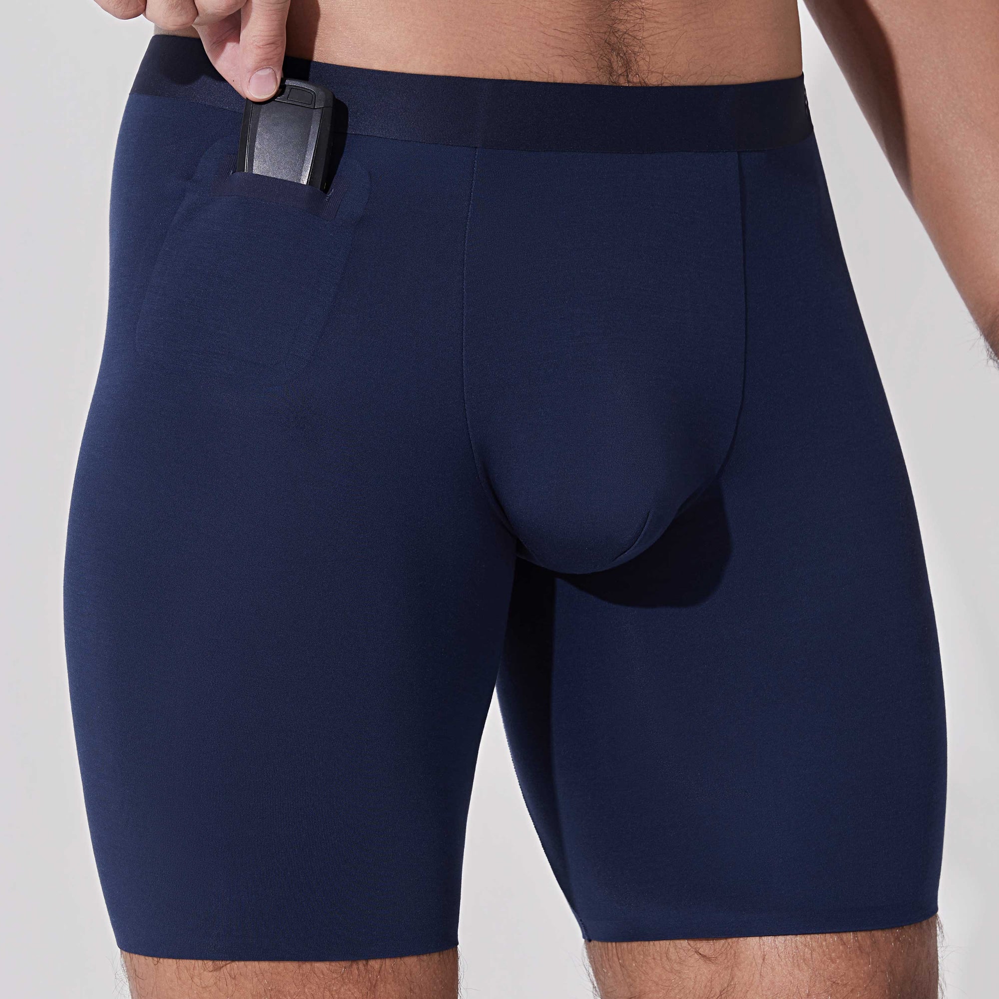 Man placing car key into pocket of navy blue boxer briefs with patented pocket