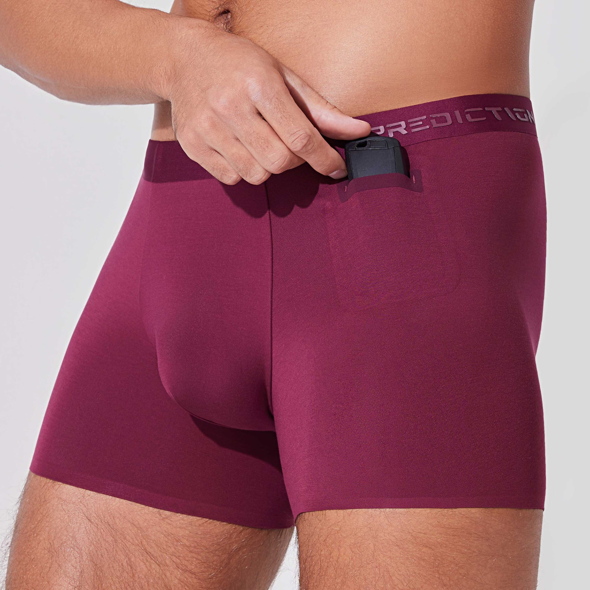 Man placing car key into pocket of burgundy boxer briefs with patented pocket