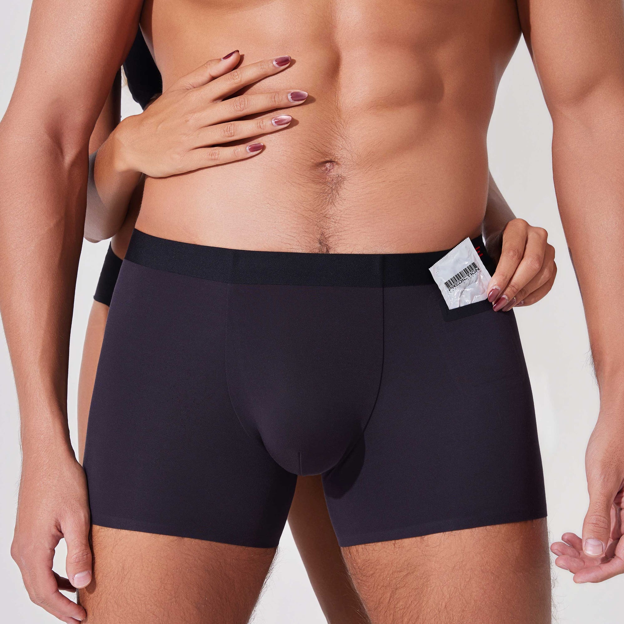 Couple placing a condom into the pocket of black boxer briefs showing functional pocket use